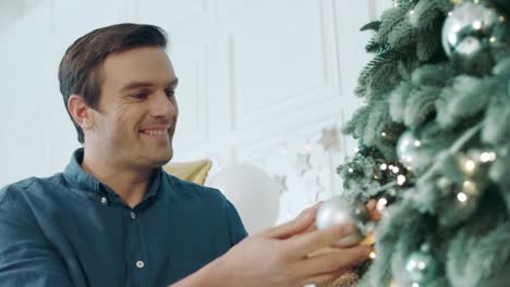 Closeup-handsome-guy-putting-silver-ball-on-green-tree.
