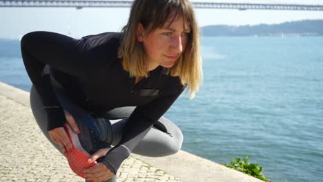 Concentrated-sportswoman-exercising-on-embankment-near-river