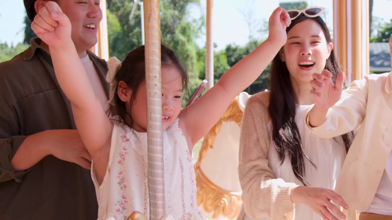 พ่อแม่และลูกสาวตัวน้อยยิ้มแย้มขณะกำลังขี่ม้าหมุนวินเทจท่ามกลางแสงแดดจ้ากลางแจ้ง
