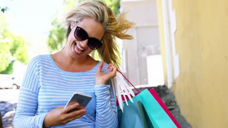 mujer sonriente usando un teléfono móvil y sosteniendo una bolsa de compras en la mano