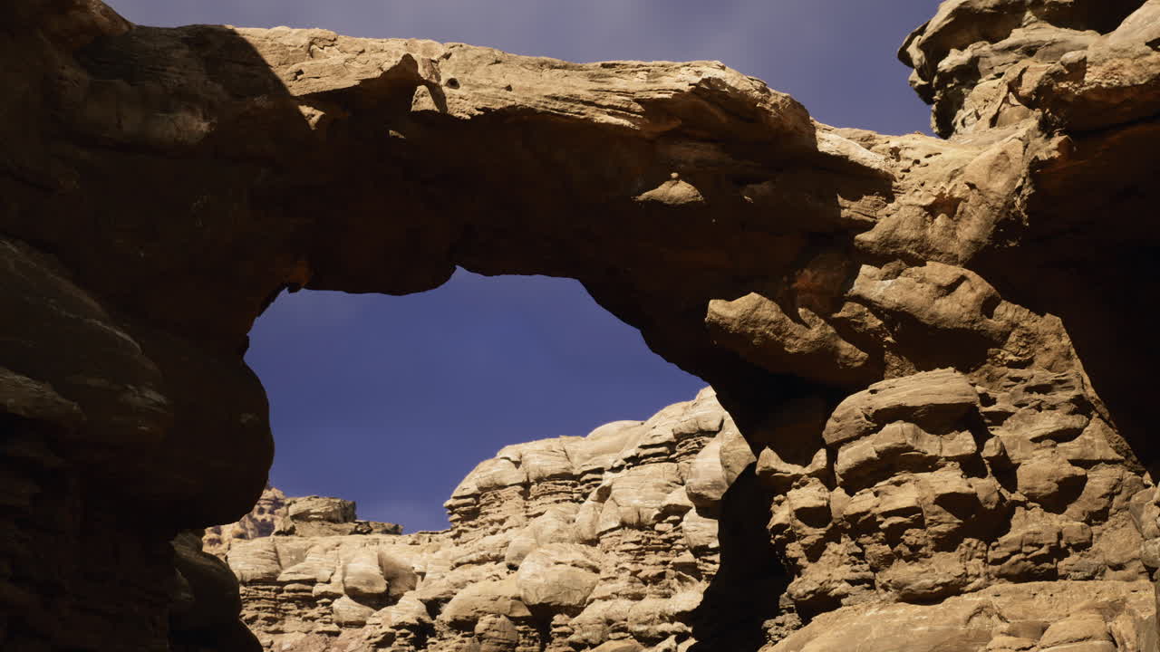 Natural stone arch formation under clear blue sky at rugged canyon