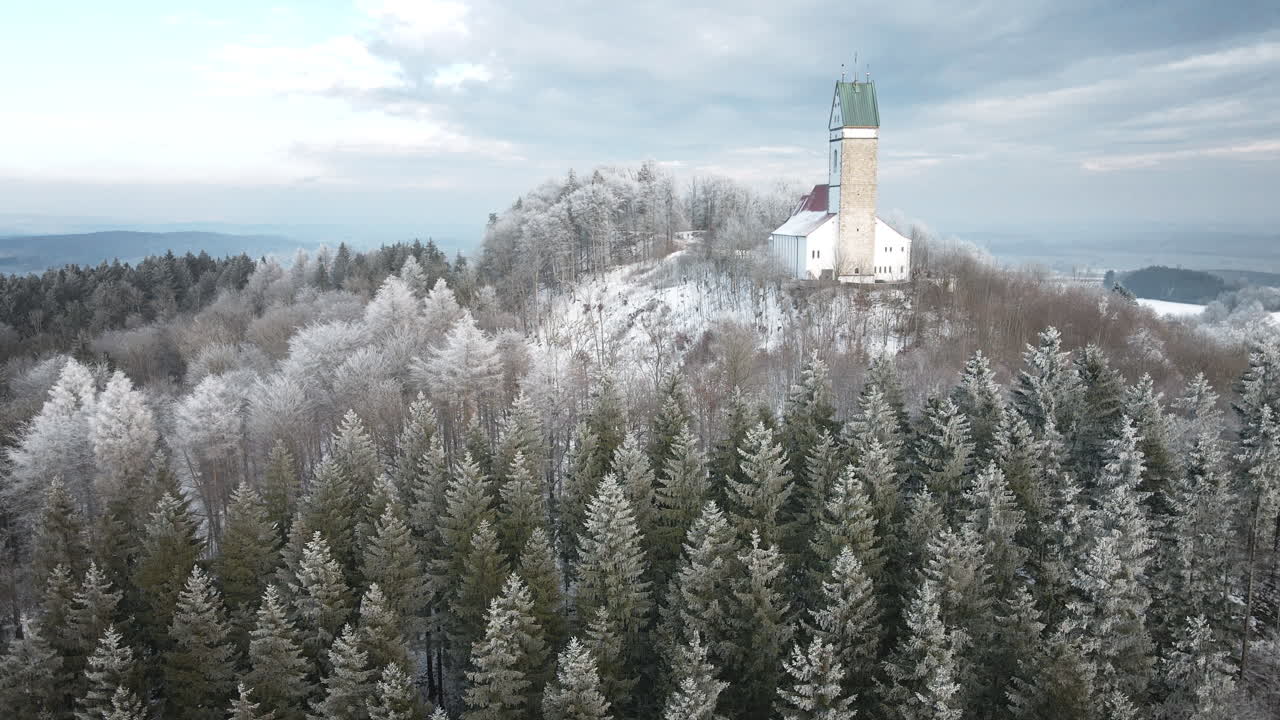 drone fremadrettet kirke, frostklar stedsegrøn skov, kapeltårn på bakketop, grønt tag vinterkirke, Utteweiler Baden Württemberg, sneklædt skråning, luftoptagelse ind, tysk vinterlandskab