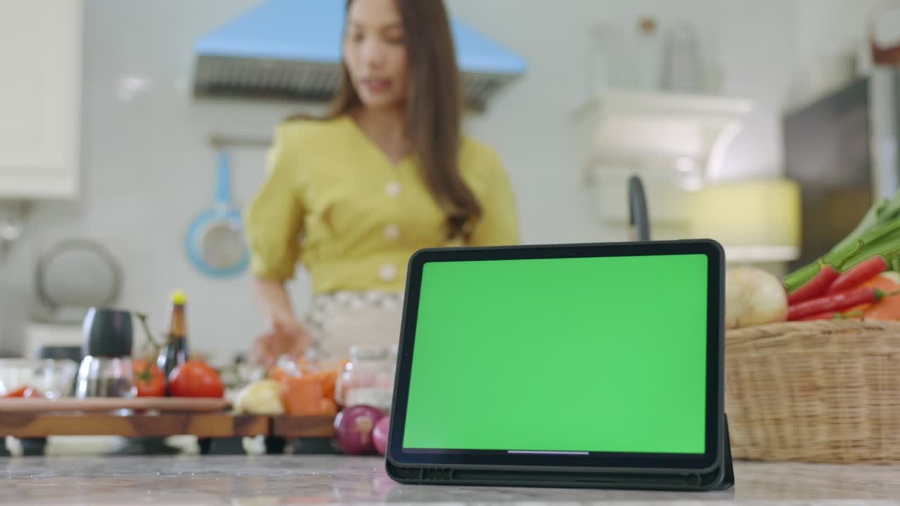 tableta con una pantalla verde con un hermoso fondo cocinando en la casa con una cara feliz, la esposa hace el desayuno felizmente en su casa.