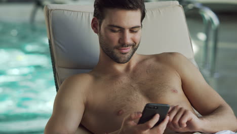 Closeup-man-looking-phone-by-pool.-Male-relaxing-with-phone-at-wellness-center