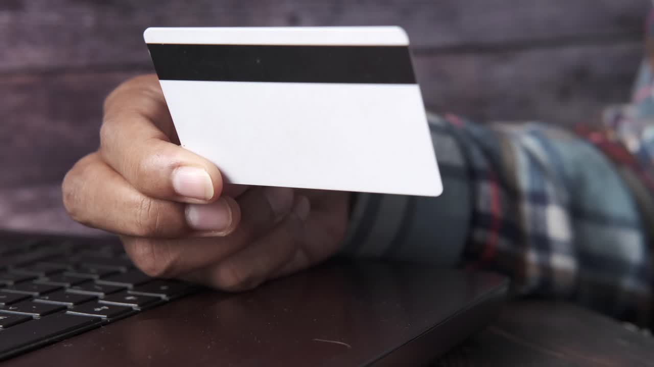 la mano sosteniendo una tarjeta de crédito sobre una computadora portátil