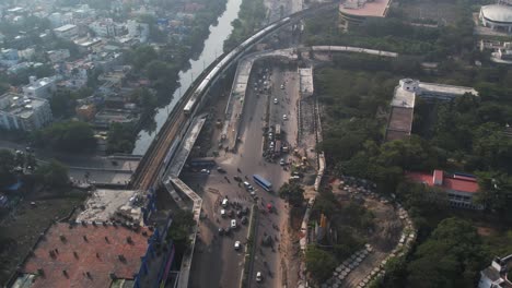 Aerial-shot-of-metro-train-passing-through-the-city,-filled-with-cars-in-the-highway-near-buildings