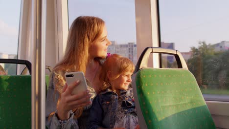 a woman and a young girl sit on a bus and look at a phone