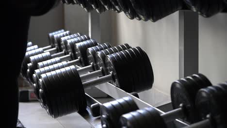 close-up of young concentrated woman with headphones lifting dumbbells in a gym by the outdoor swimming pool on the background, slow motion