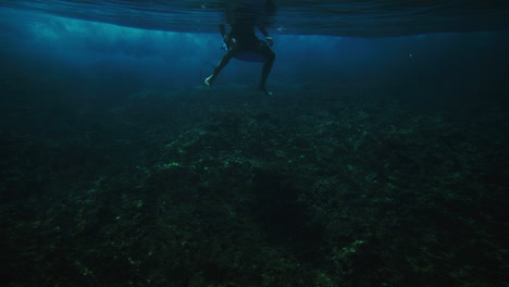 Surfer-calmly-sits-looking-at-crashing-wave,-view-from-underwater-surface-above-reef