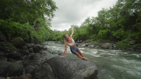 fit sportive young woman doing side plank pose on rock beside river, vasisthasana