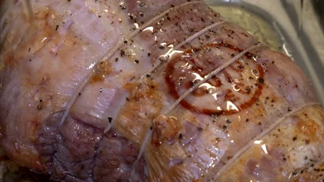 slow motion close up of pouring oil on top of a halfway cooked a joint of pork in a glass oven dish