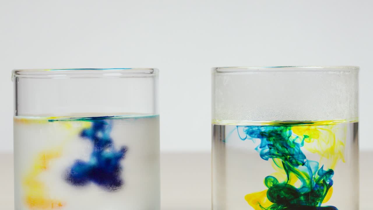 Pipettes release colored dye into clear water, showing diffusion in glass containers under bright lighting