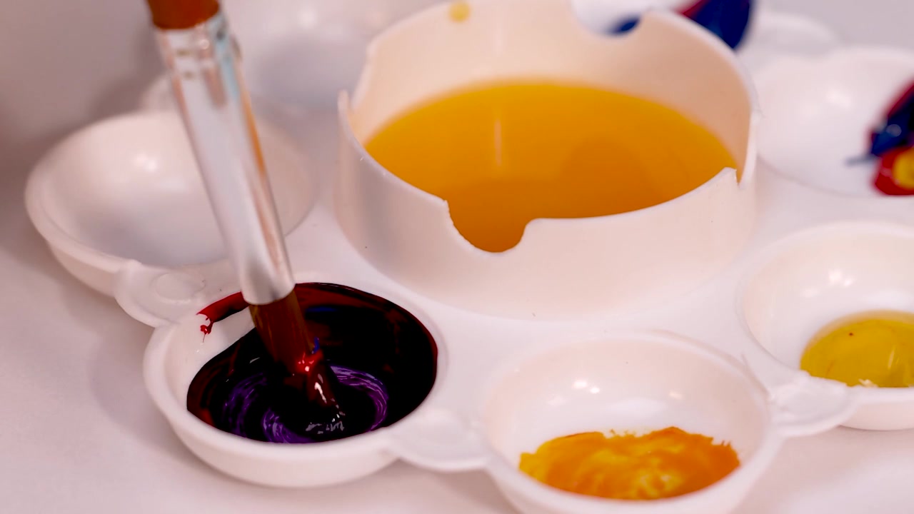 Primo piano di pennello che mescola pittura viola e nera su una tavolozza.