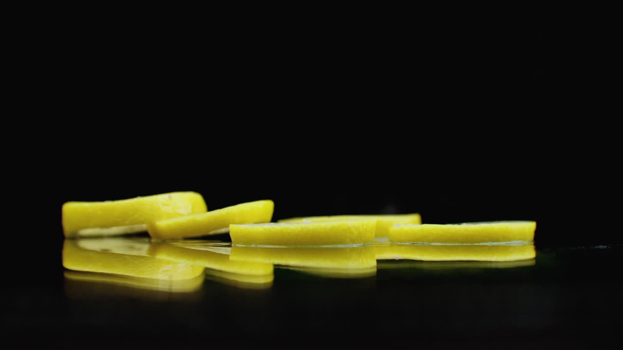 Slow motion. Sliced ​​lemon rings fall with splashes of water on the glass on a dark background. Cut into slices.