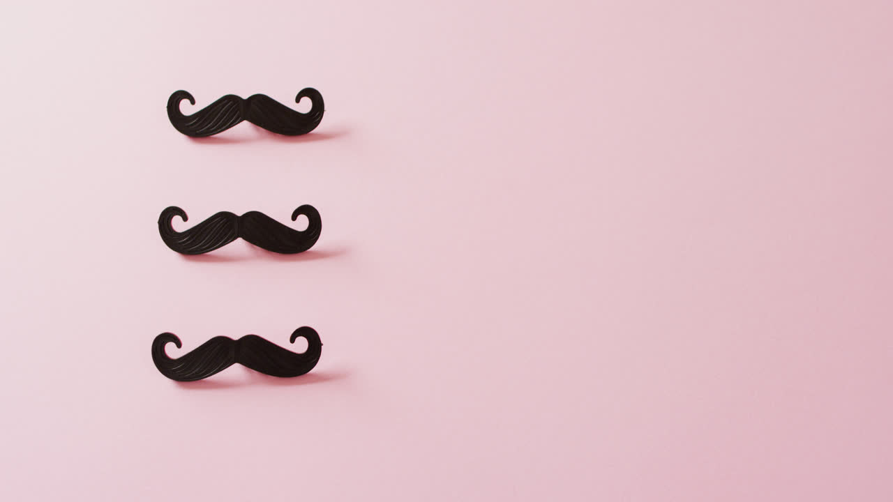Video of three black false moustaches on pink background with copy space