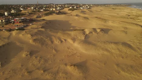 wide drone shot of a couple walking beach by dunes at sunset