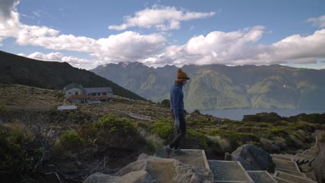 Pan,-hikers-descends-steps-towards-Luxmore-Hut,-distant-mountain-landscape,-Kepler-Track-New-Zealand