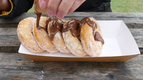 Pouring-chocolate-sauce-on-sugared-donuts