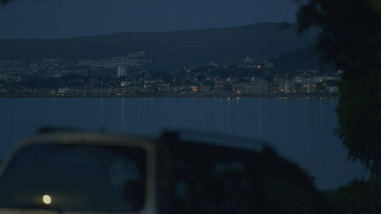 lejana ciudad costera con agua y coche borroso en primer plano, luz de la noche