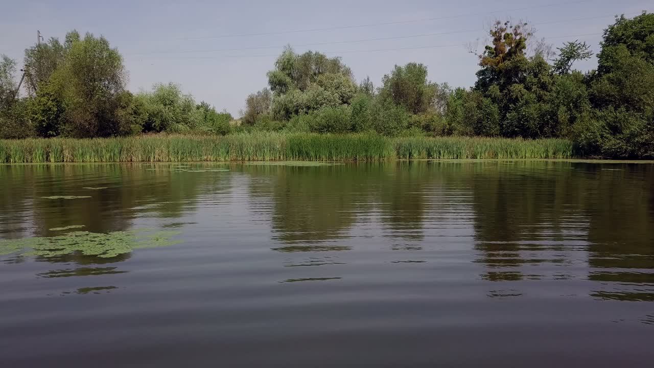 Flying over the river with calm water into the natural green background of trees and comedians. Beautiful view of river with the reflection of trees in the water in summer.