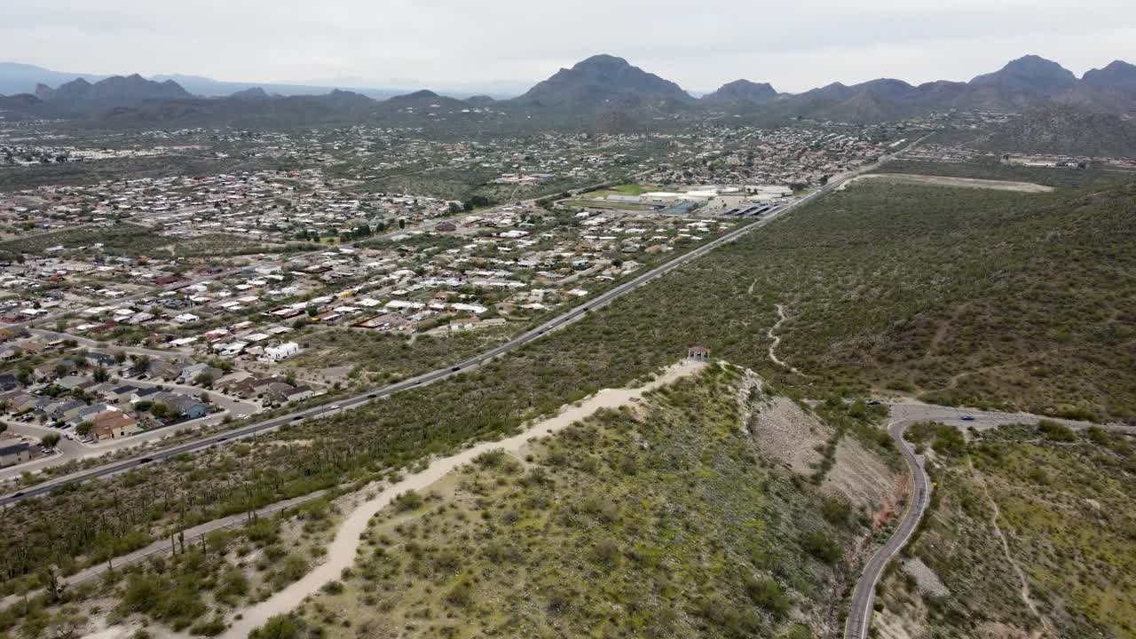 Vista aerea con drone di Tucson, Arizona, che mostra colline desertiche e catene montuose che delimitano quartieri periferici e l'aperto paesaggio del deserto di Sonora sotto cieli nuvolosi
