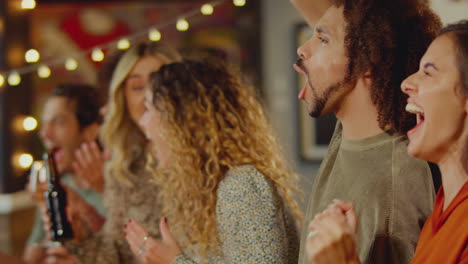 group of friends celebrating watching sports game or match drinking in bar together