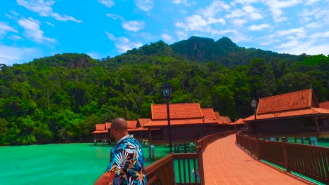 a relaxed man on a stilt of a luxury hotel looks out to sea in langkawi island