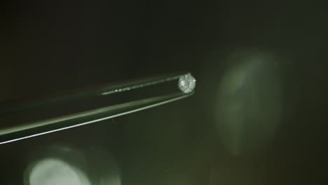 close up shot of a real diamond getting held by a pair of tweezers with a blurry bokeh background and shiny reflected light log