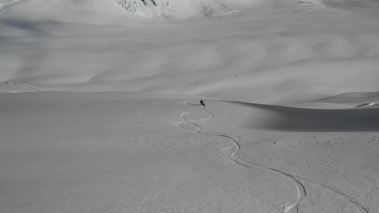 4K drone footage of snowboarder going down big empty slope