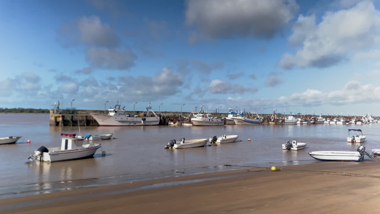 Barche da pesca ormeggiate lungo un molo e piccole barche a motore ferme sulle rive sabbiose del fiume Guadalquivir a Sanlúcar de Barrameda.