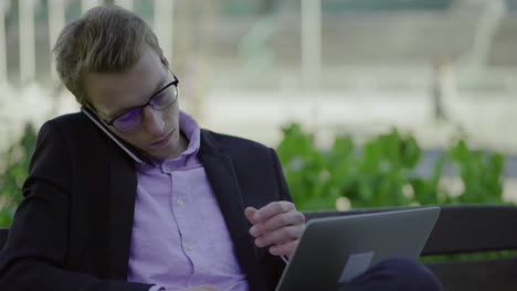 Focused-man-typing-on-laptop-during-conversation-through-phone