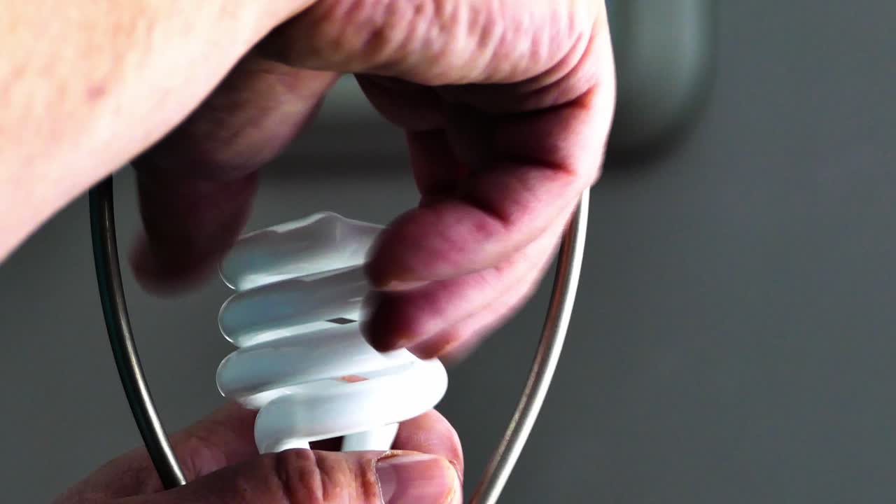 A close‑up shot of a hand carefully removing an old incandescent bulb and replacing it with a modern energy‑saving LED bulb