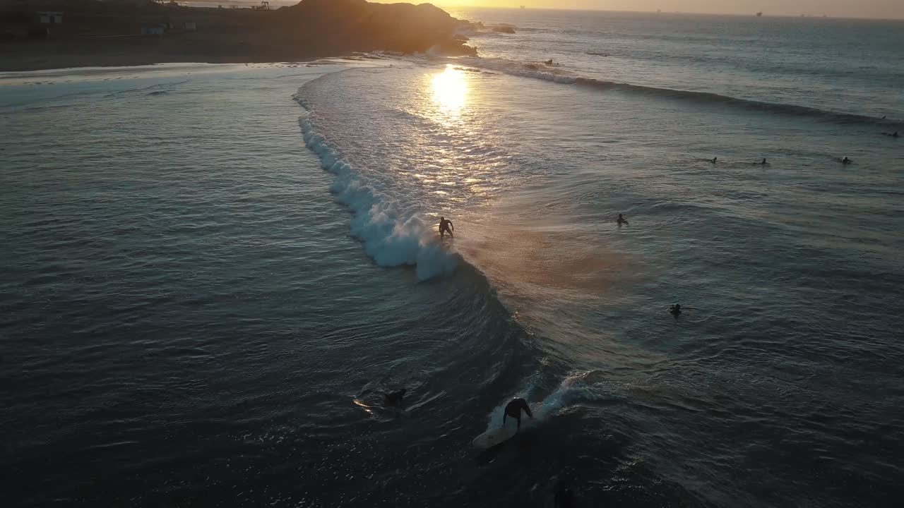 Beautiful drone aerial of people surfing in the ocean of Peru during Sunset