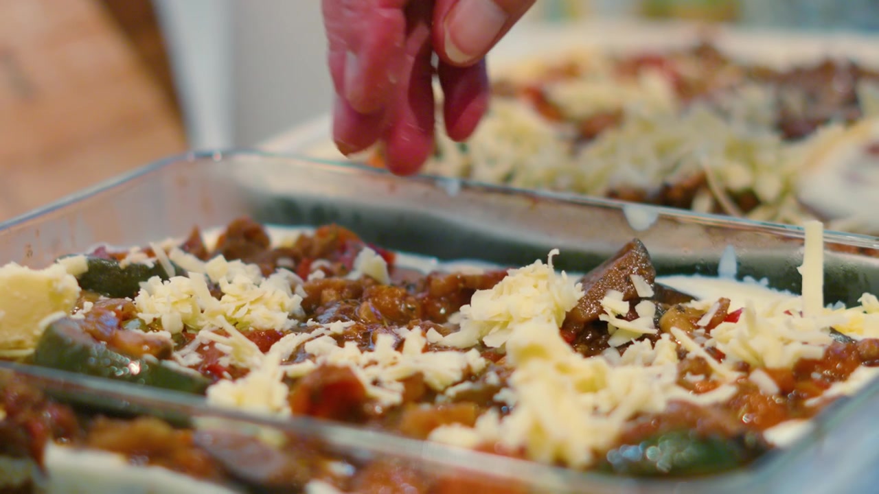 Mano femminile che lascia cadere il formaggio sullo strato di ragù alla bolognese mentre prepara la pasta per la lasagna italiana in slow motion. Filmato di cucina, preparazione del cibo 4K