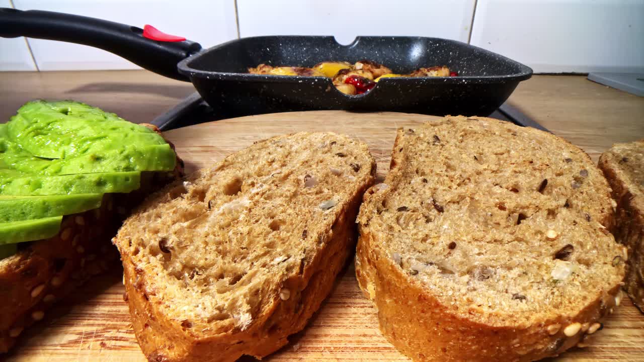 Close up of hand placing sliced avocado on whole grain bread in home kitchen