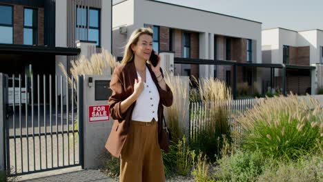 donna che parla al telefono vicino a una casa in vendita