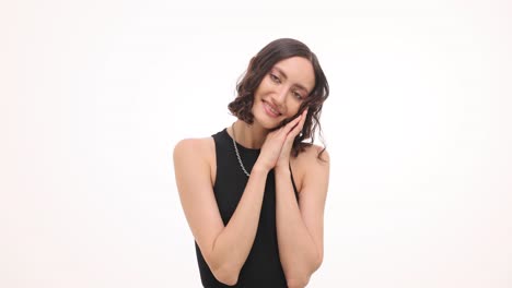 a happy young woman with curly hair poses with clasped hands against a white background