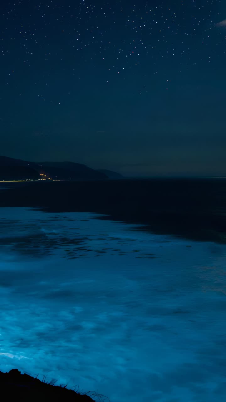 Video verticale: mare luminescente che si muove mentre le onde si infrangono sulla riva, mescolando il plancton, scogliera