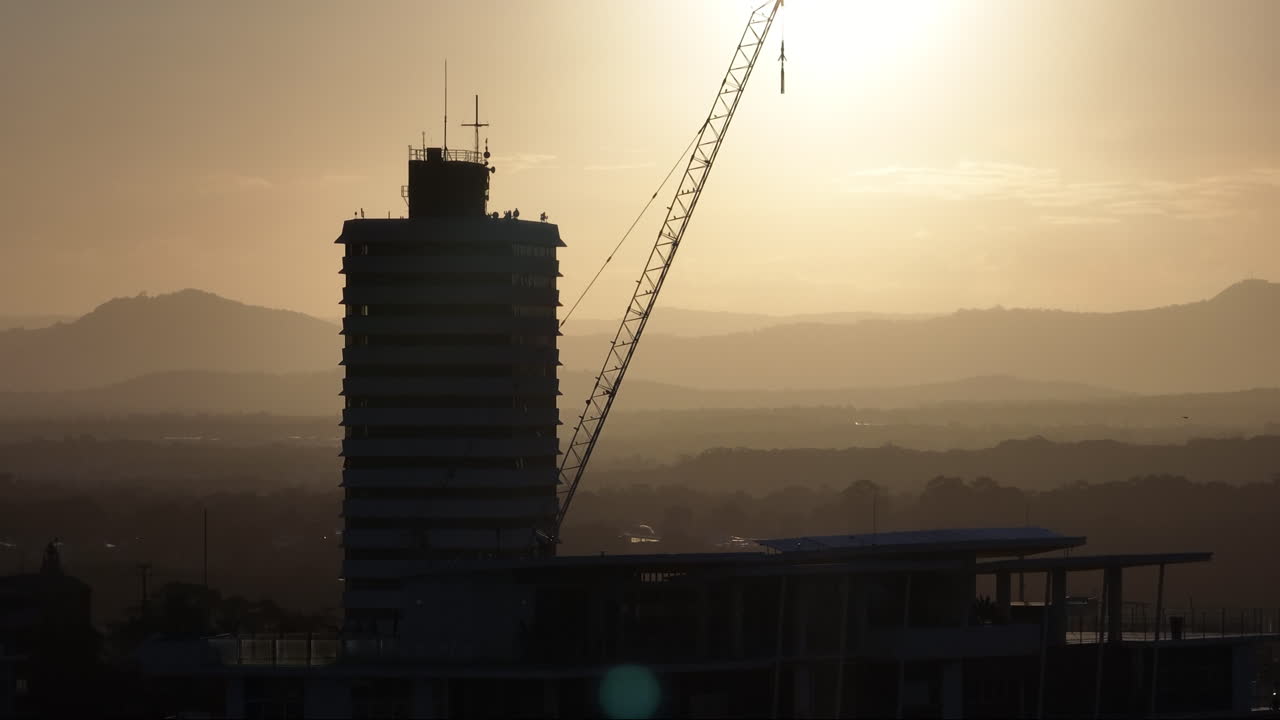 edificio de paralaje de teleobjetivo de avión no tripulado con silueta de grúa al atardecer, 4k