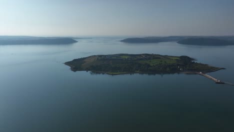 spike island, county cork, ireland, september 2024. drone approaches fort mitchel as soft hazy light diffuses through clouds of vegetated island prison.