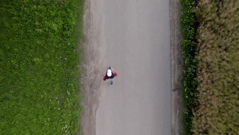 Top-down-aerial-view---A-jogger-running-on-a-narrow-paved-road-between-grasses-and-farmland