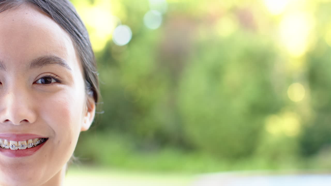 Smiling asian girl with braces enjoying outdoors, close-up portrait in natural light, copy space