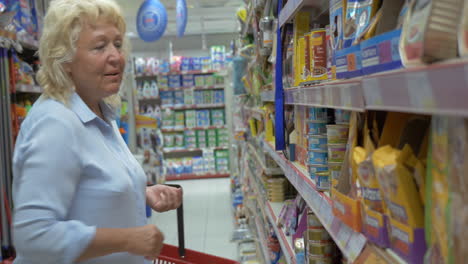 La-Mujer-Mayor-Está-Eligiendo-Alimentos-Enlatados-Para-Mascotas-En-El-Pasillo-Del-Supermercado-Con-Una-Cesta-De-La-Compra.