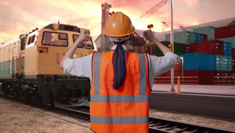back view of a female engineer with safety helmet raising her hands celebrating while working with freight cargo train at port