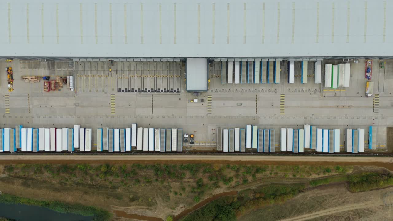 Drone footage looking straight down on distribution warehouses in Bedford, with trucks parked and trailers unloading under clear daylight