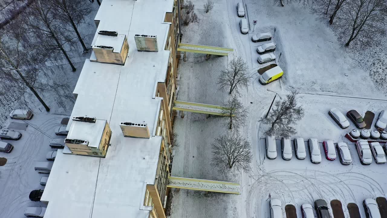 Snow covering a residential building, bare trees, and many cars in multiple car park spots in aerial view