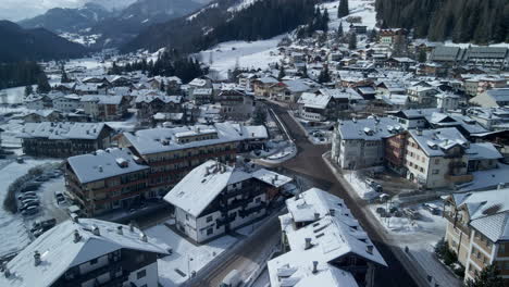 Winter-cityscape-in-Val-di-Fassa,-Italy:-aerial-view-flying-over-snow-covered-buildings-in-4k