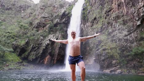 young blond man poses below fundao waterfall in remote brazil landscape