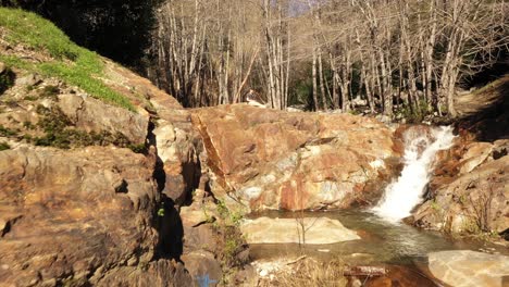 Slow-pan-of-a-young-white-male-hiker-sitting-atop-of-Etiwanda-Falls-in-Rancho-Cucamonga-and-San-Bernardino,-California-in-morning-light-with-cascading-waterfalls,-graffiti-and-foliage