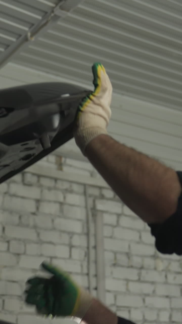 mecánico en uniforme azul cierra con seguridad el capó de un coche negro dentro de un taller mecánico, asegurando que todas las comprobaciones de mantenimiento se completen
